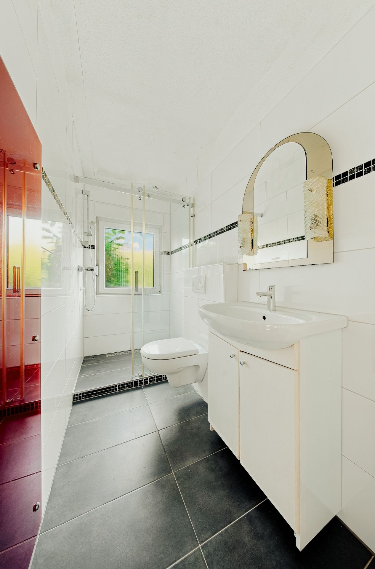 Modernes Bad mit Hängetoilette, Waschbecken, Spiegel und ebenerdiger Dusche mit Glaswand.