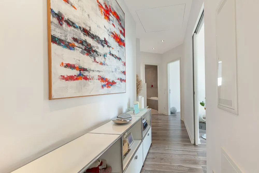 Heller Flur mit modernem Bild, Sideboard und Türen zu weiteren Räumen.