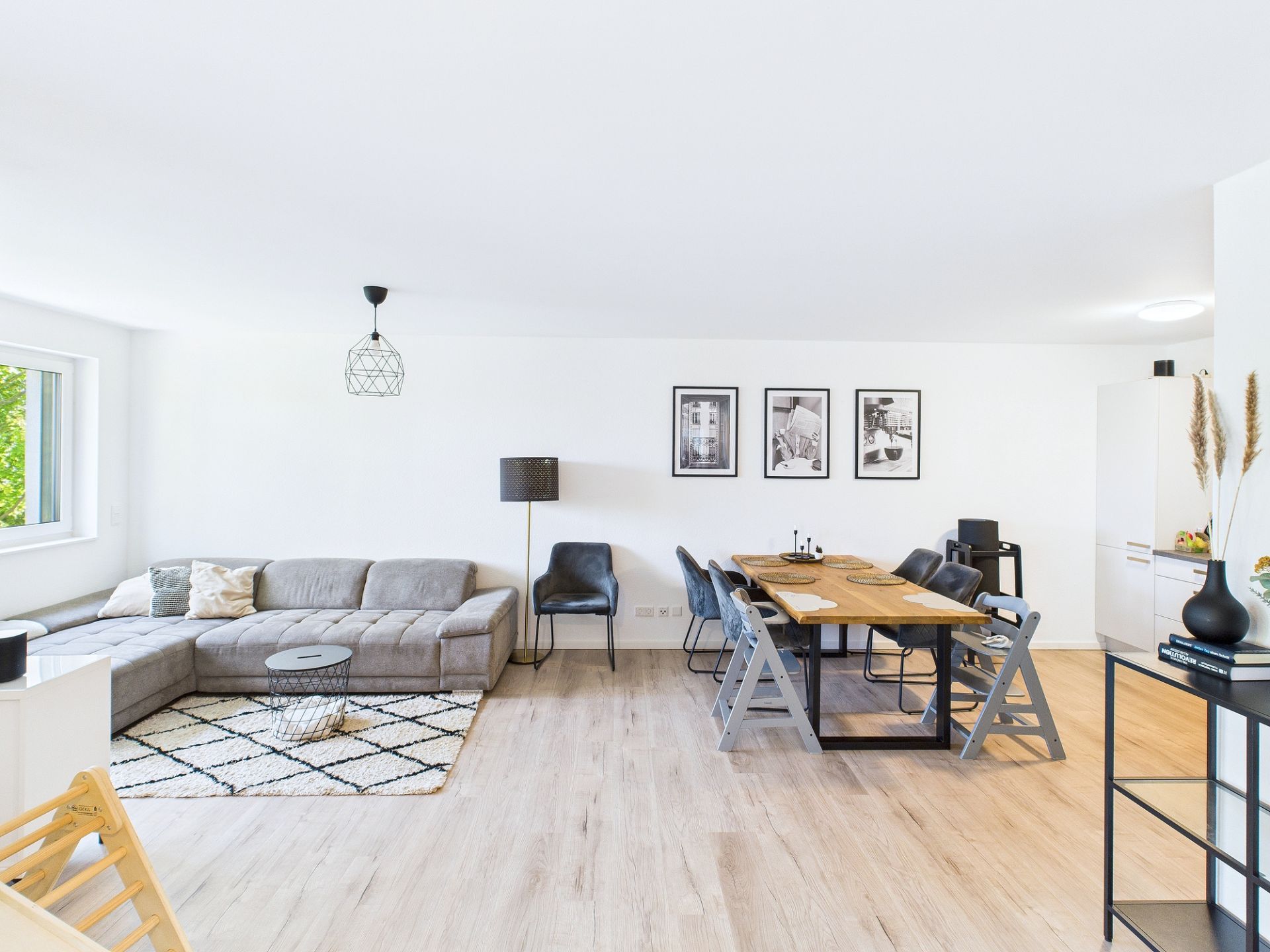Helles Wohnzimmer mit grauem Sofa, Esstisch, Stühlen und Dekoration an der Wand.