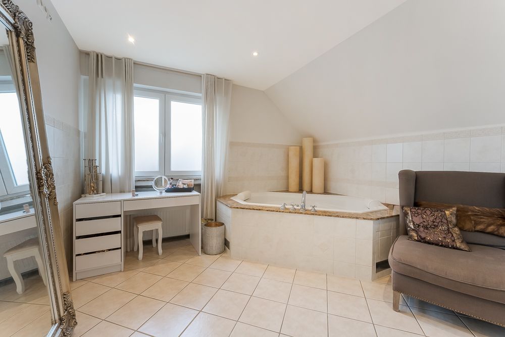 Helles Badezimmer mit Eckbadewanne, großem Spiegel, Schminktisch und Sessel.