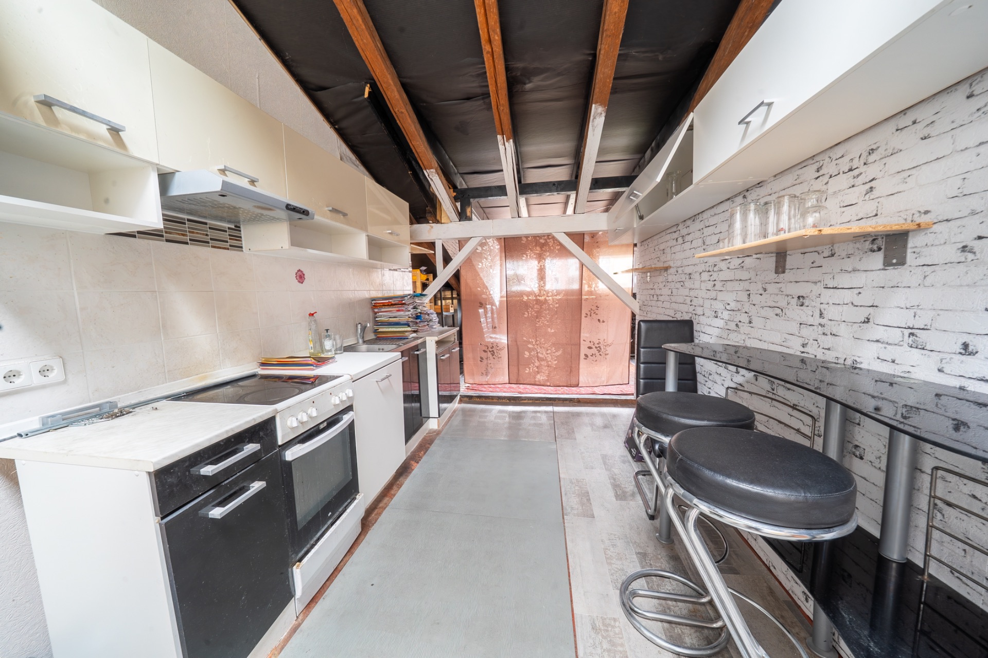 Schmale Küche mit Bartresen, schwarzen Hockern und sichtbaren Holzbalken an der Decke.