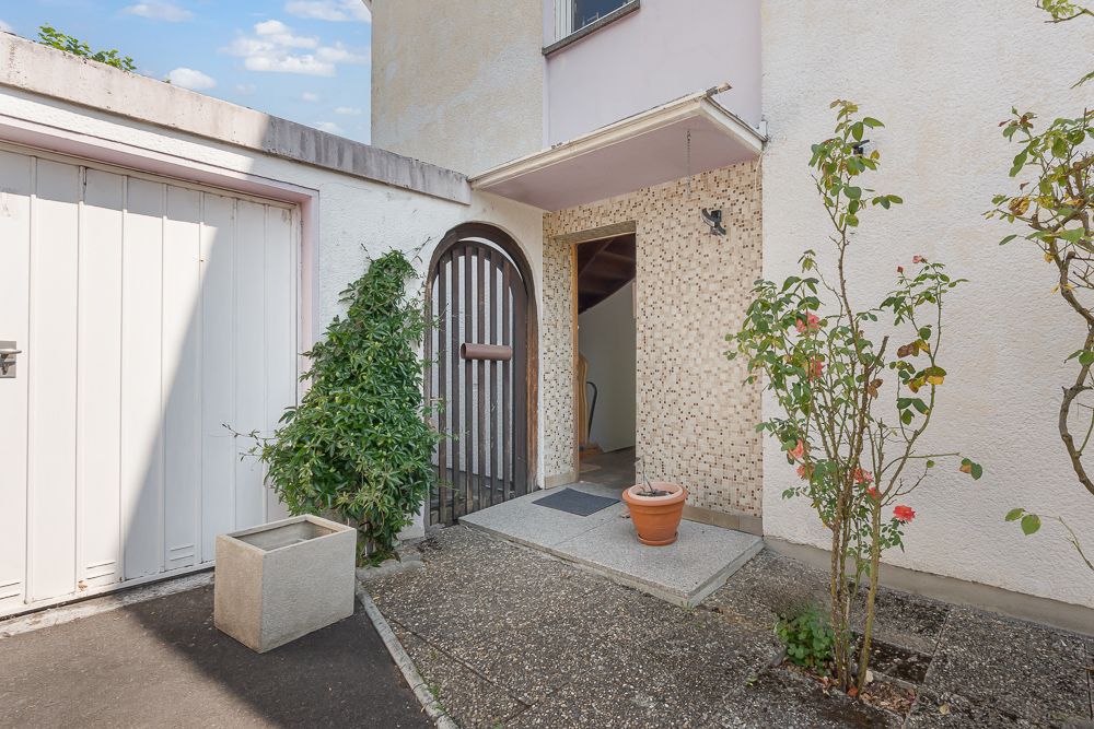 Eingangsbereich mit kleinem Tor, Topfpflanzen und Garage an einer Wohnhausfassade.