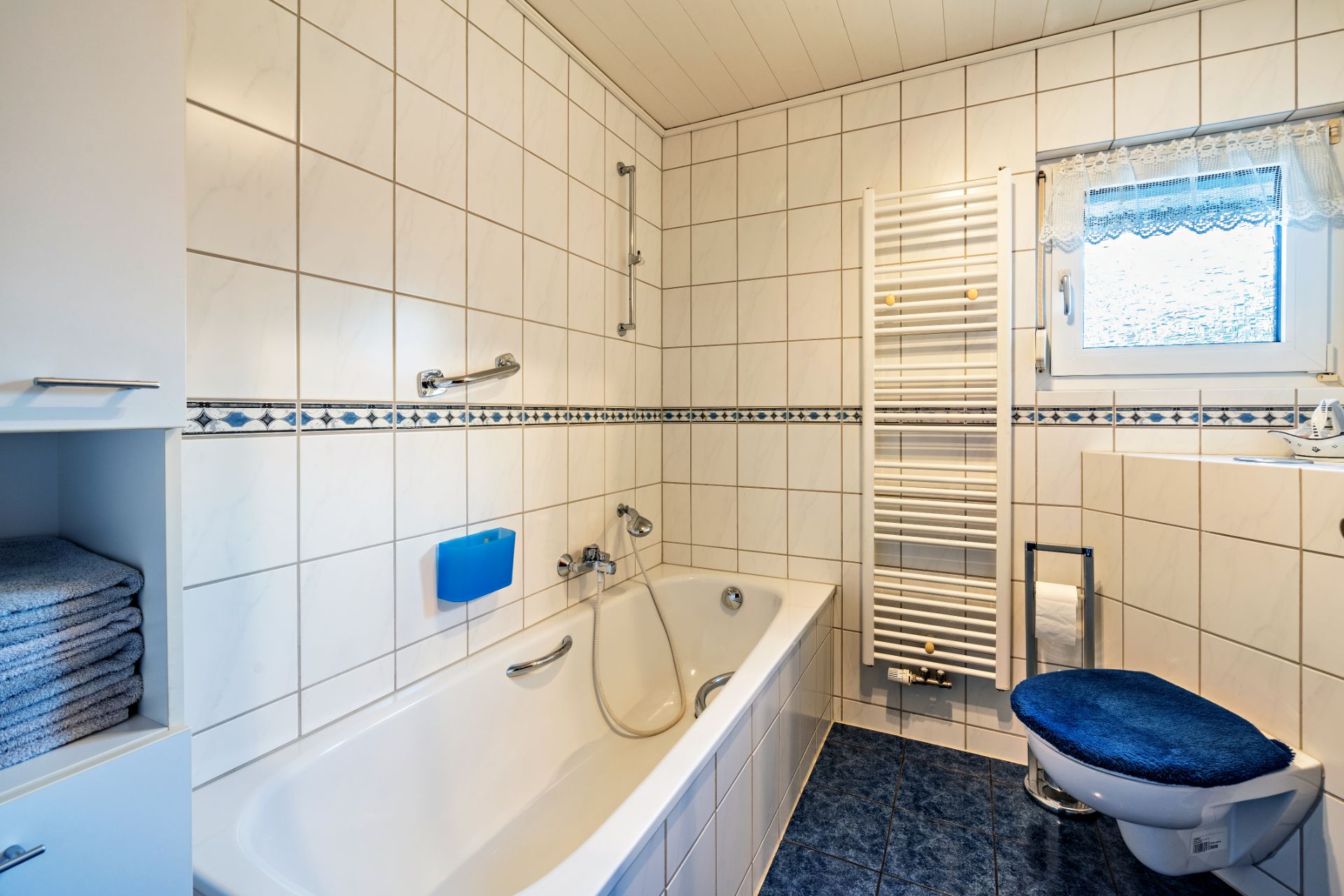 Helles Badezimmer mit Badewanne, Toilette, Handtuchheizkörper und kleinem Fenster.