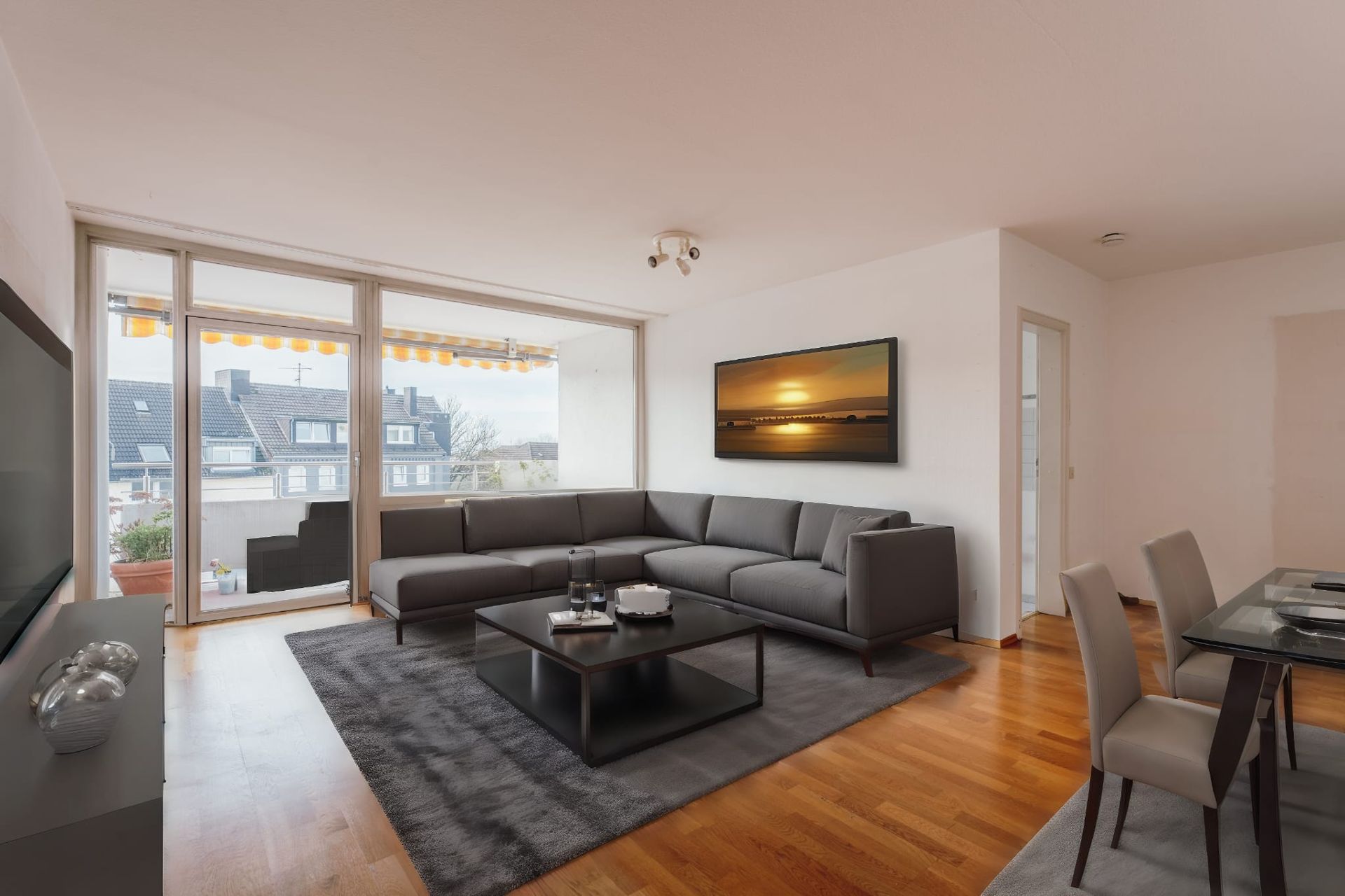 Modernes Wohnzimmer mit grauem Ecksofa, Couchtisch und großem Fenster mit Balkonzugang.