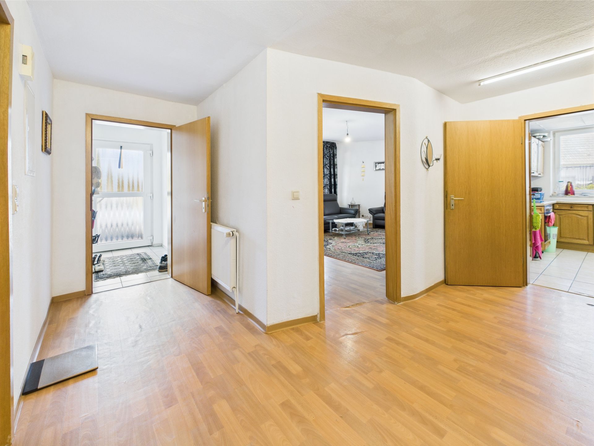 Heller Flur mit Holzboden, mehrere offene Türen zu Wohnzimmer, Küche und Eingangsbereich.