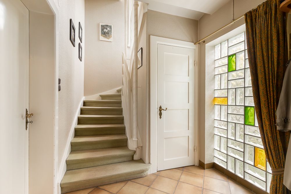 Heller Flur mit Treppe, Tür und Glasbausteinwand mit bunten Akzenten.