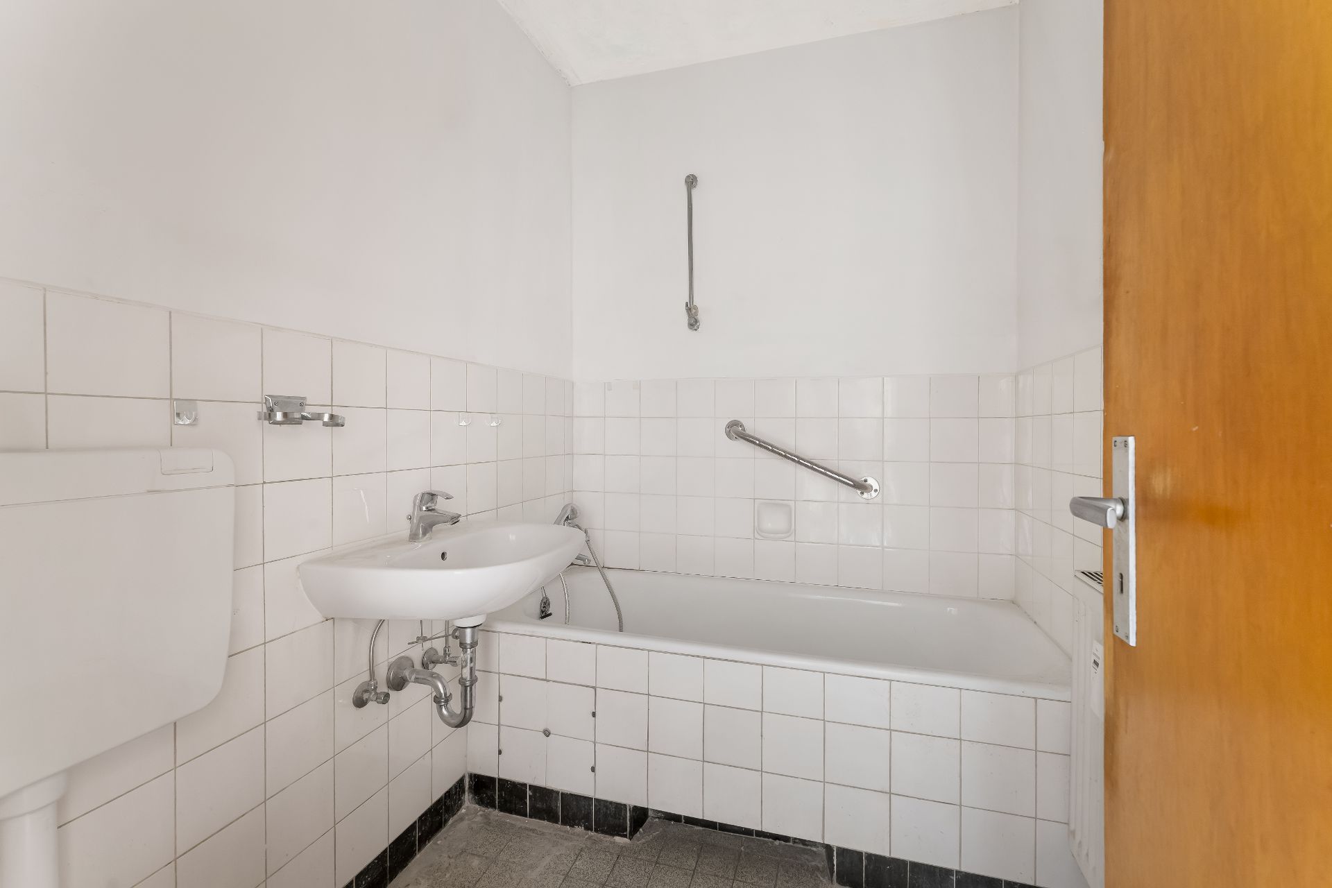 Kleines Badezimmer mit weißer Badewanne, Waschbecken und Haltegriff an der Wand.