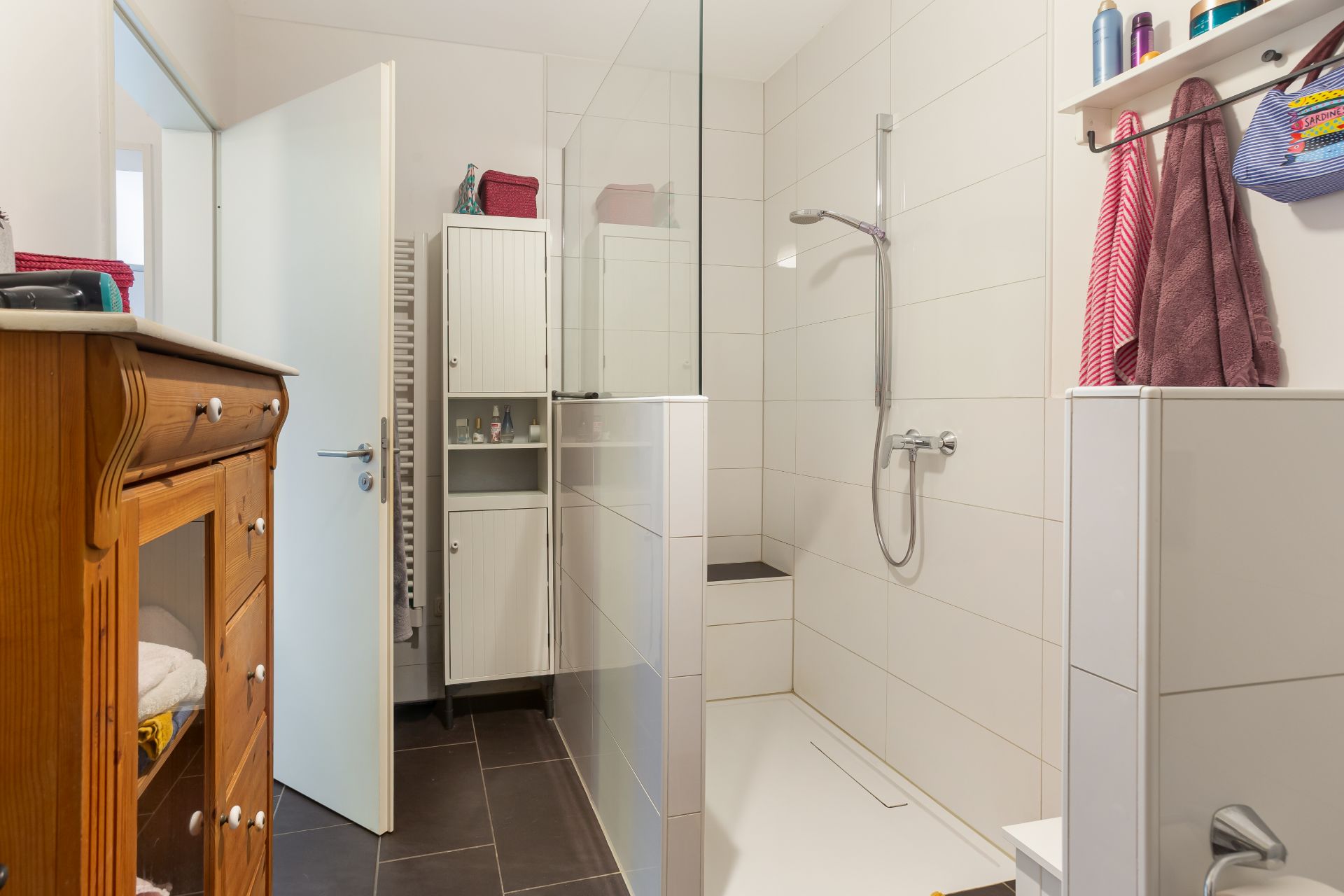 Modernes Badezimmer mit ebenerdiger Dusche, Holzschrank und weißen Fliesen.