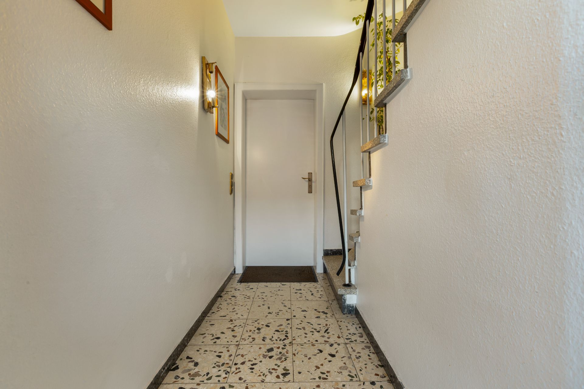 Heller Flur mit gefliestem Boden, weißer Tür und Treppe auf der rechten Seite.