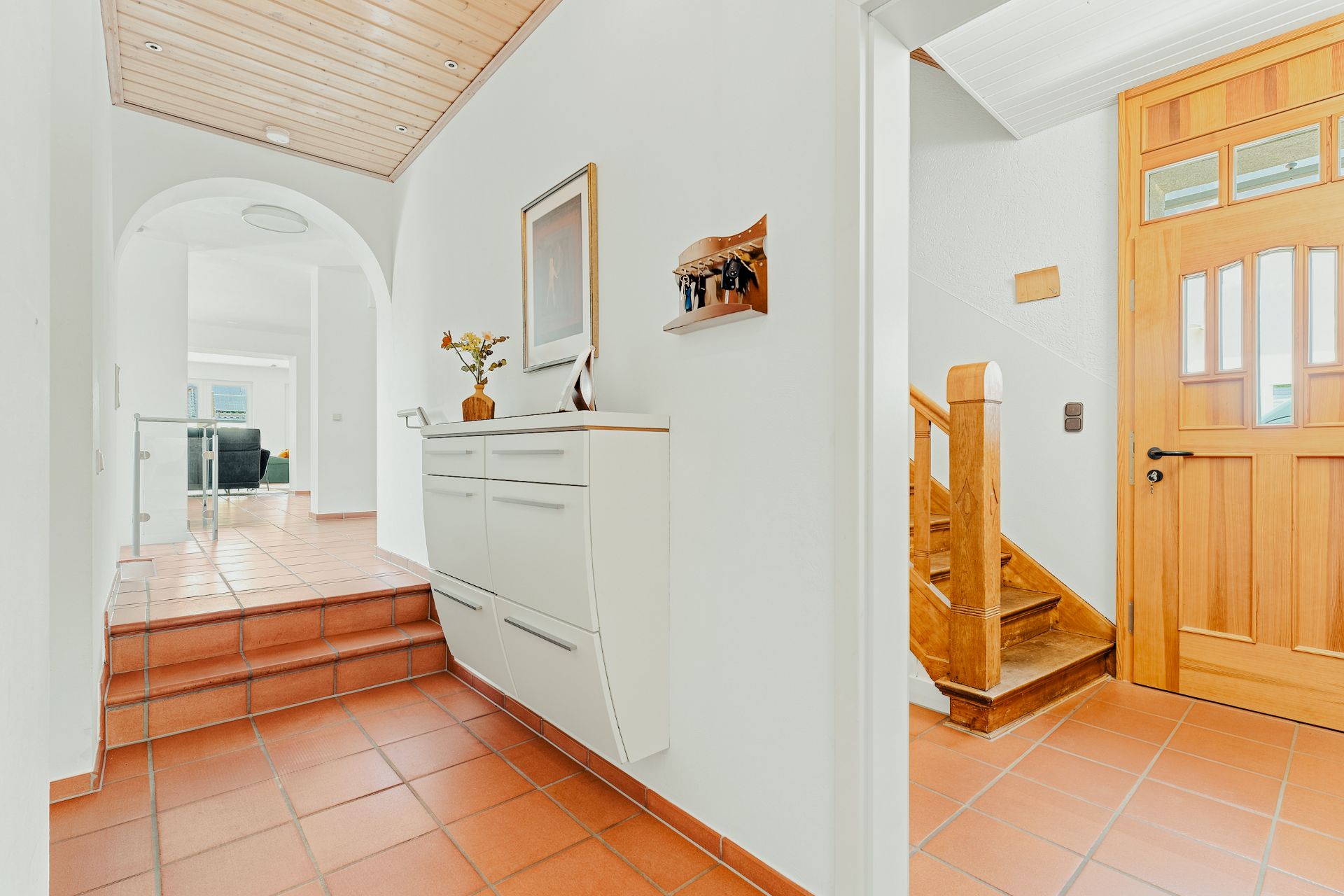 Heller Flur mit Terrakottafliesen, Holzdecke, Kommode und Treppe aus Holz.