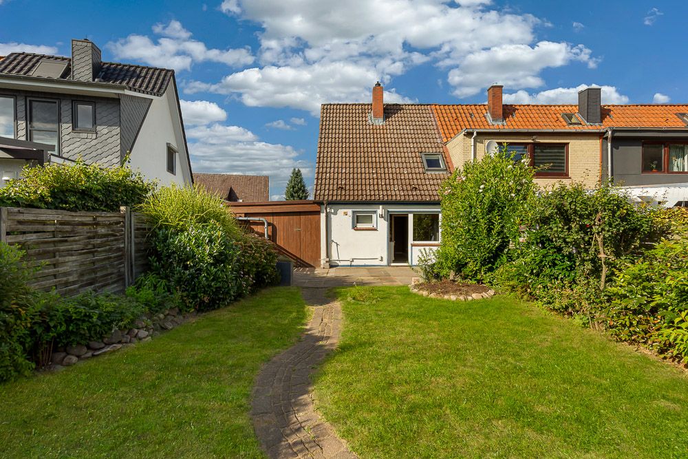 Garten mit Rasen, Weg und angrenzendem Reihenhaus bei sonnigem Wetter.