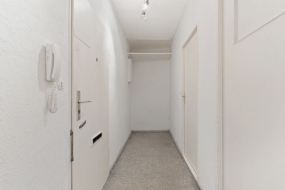 Heller Flur mit weißer Eingangstür, Gegensprechanlage und zwei weiteren Türen.