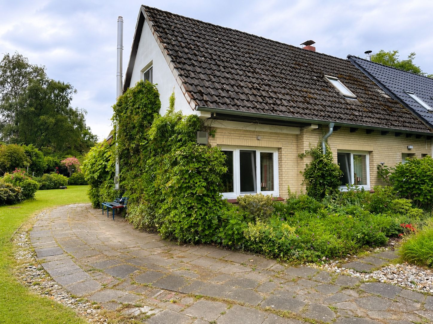 Einfamilienhaus mit Garten, bewachsene Fassade und gepflastertem Weg.
