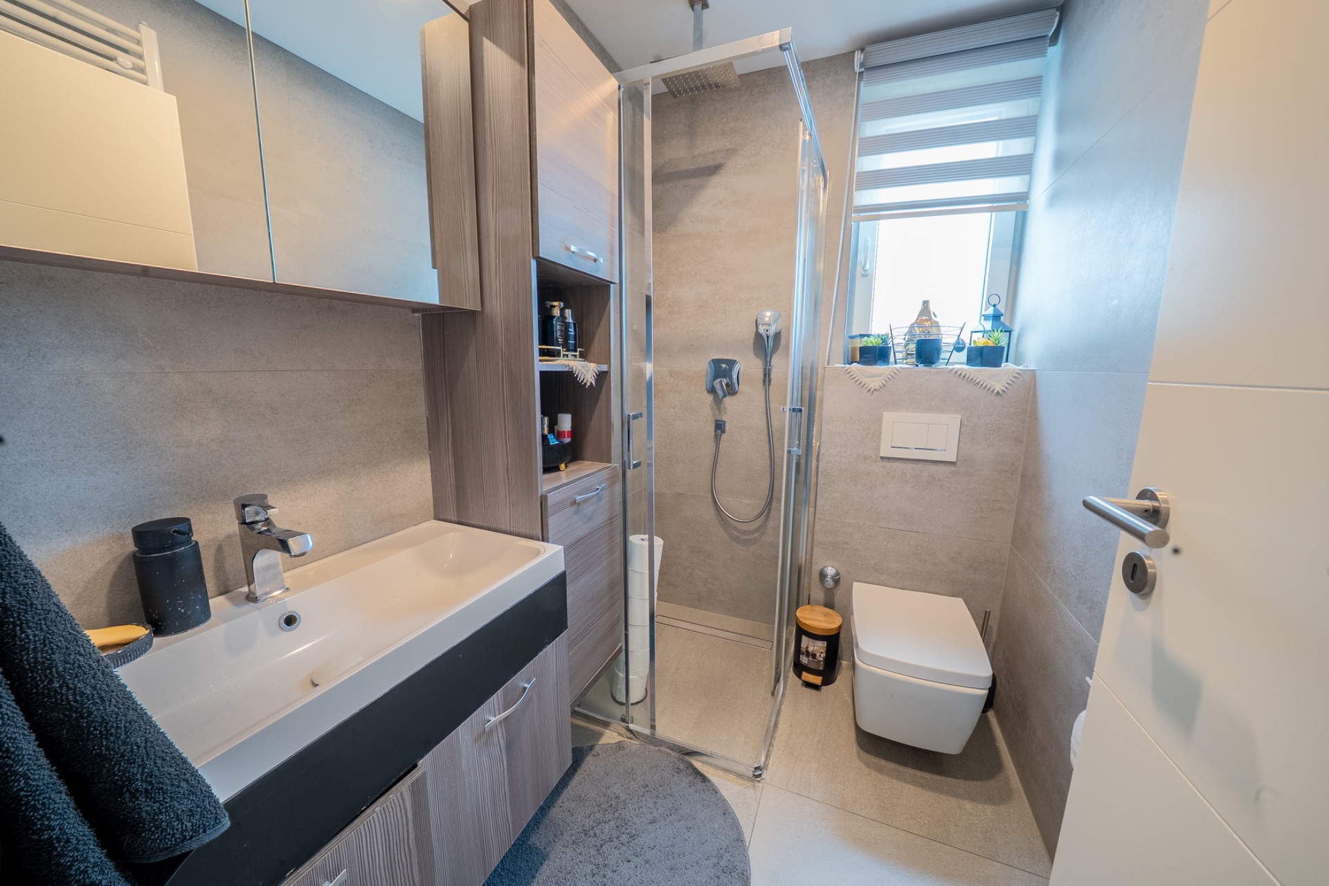 Modernes Badezimmer mit Waschbecken, Dusche, WC und Fenster.