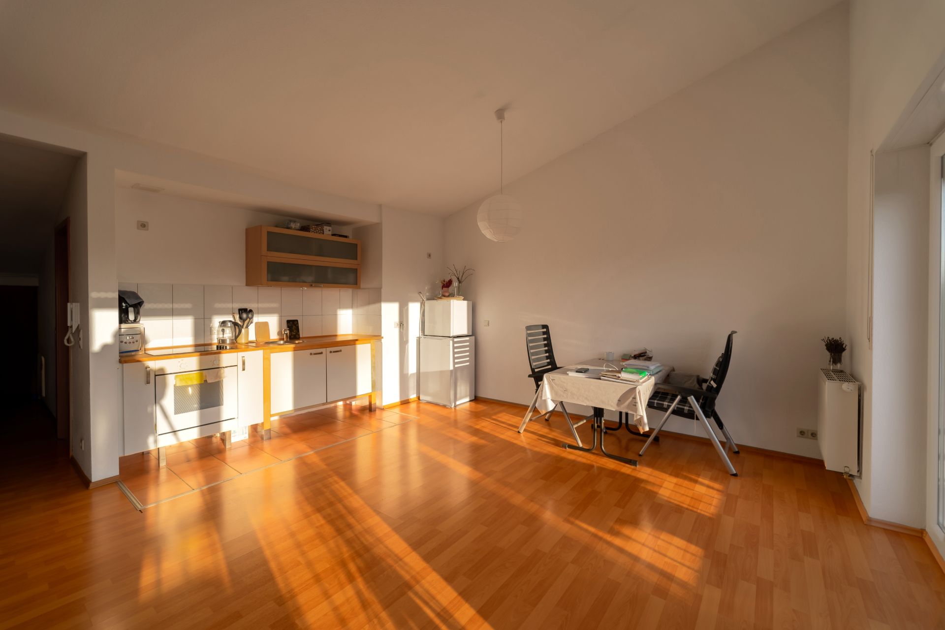Helles Zimmer mit Holzboden, Küchenzeile und Esstisch mit zwei Stühlen.