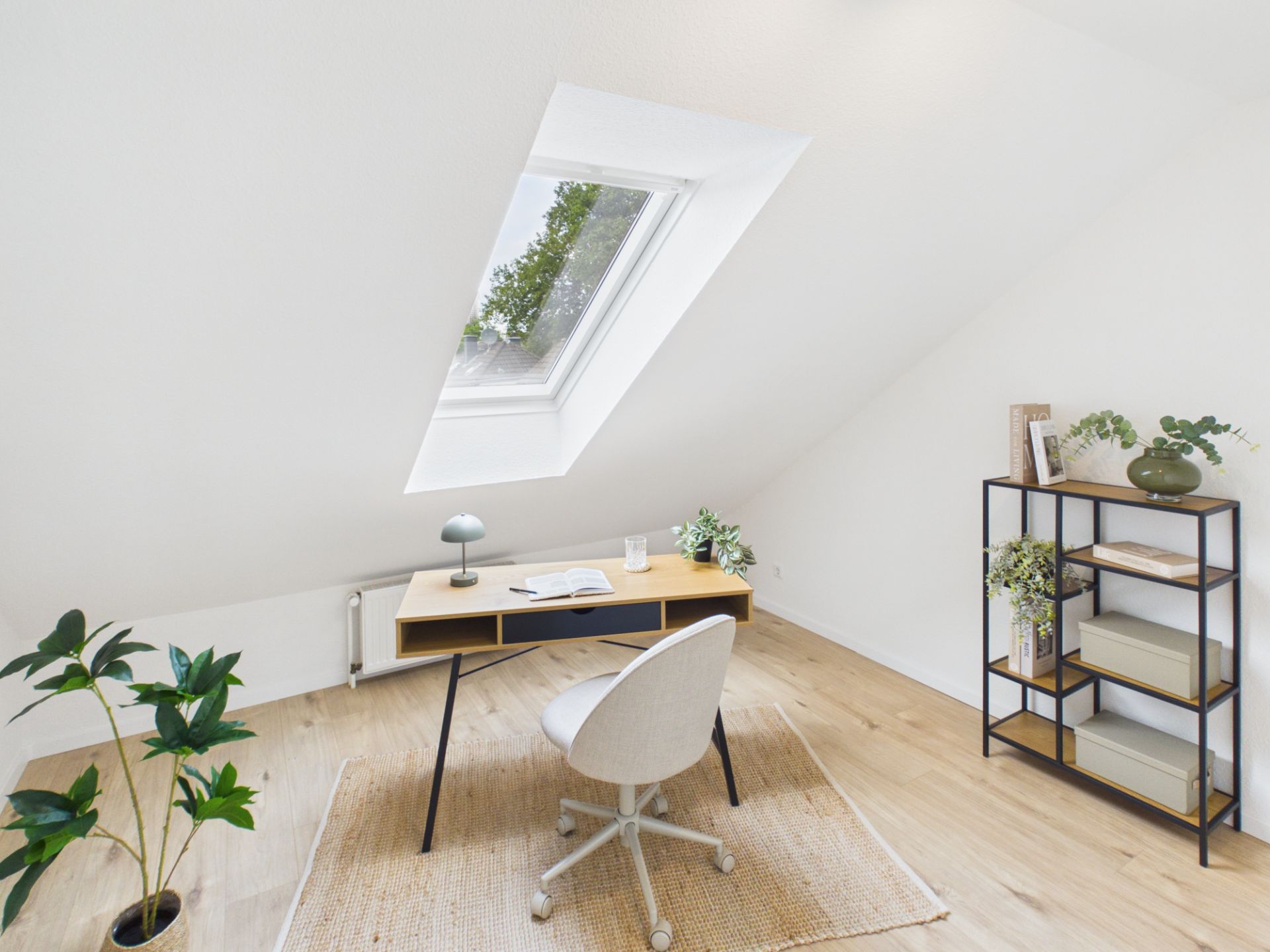 Helles Arbeitszimmer mit Schreibtisch unter einem Dachfenster und Regal an der Wand.