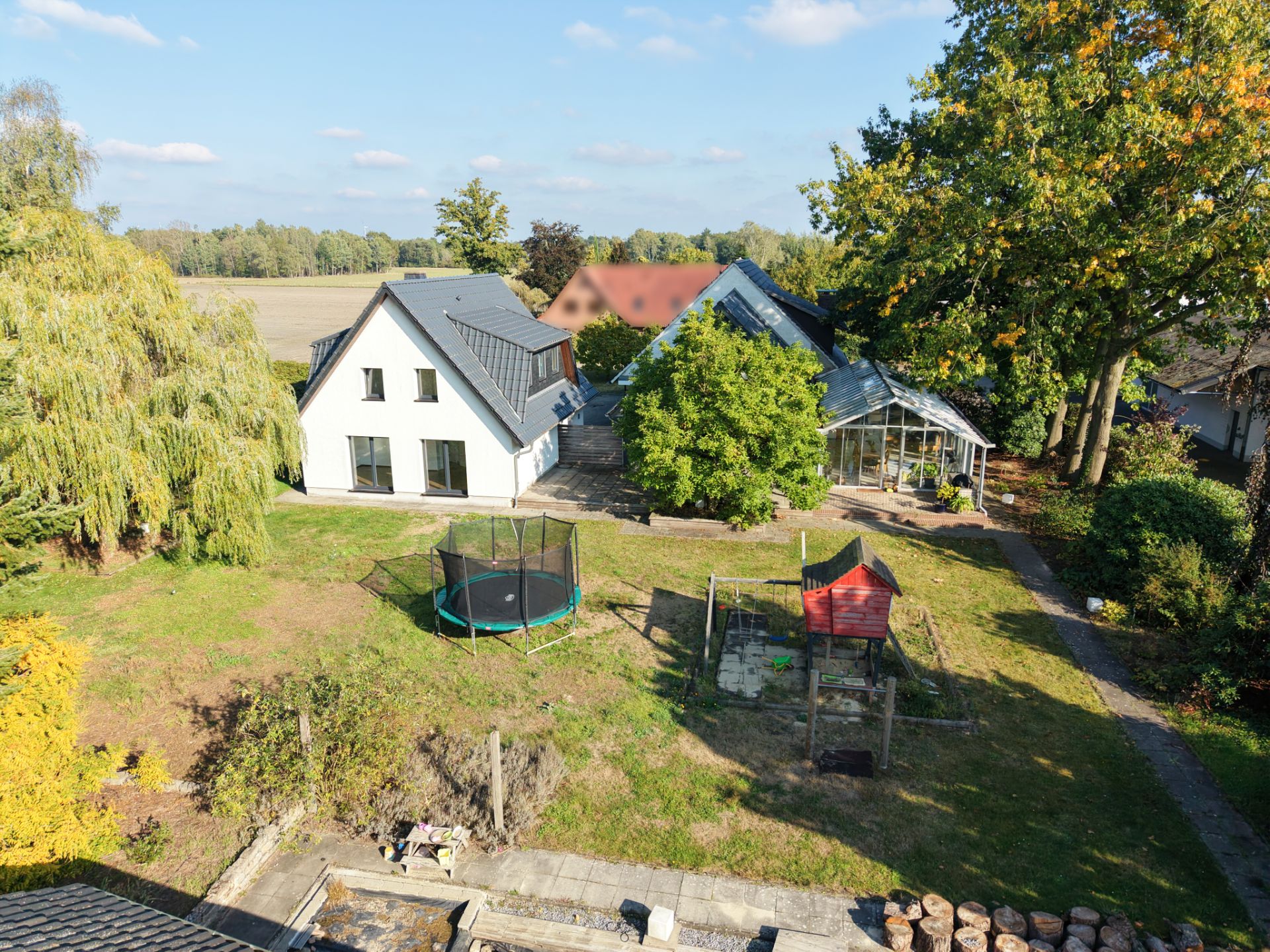 Großer Garten mit Trampolin, Spielhaus und zwei Wohnhäusern im Hintergrund.