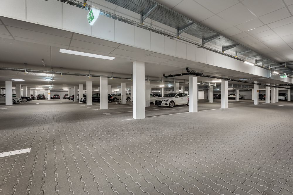 Helle Tiefgarage mit mehreren geparkten Autos und weißen Säulen.