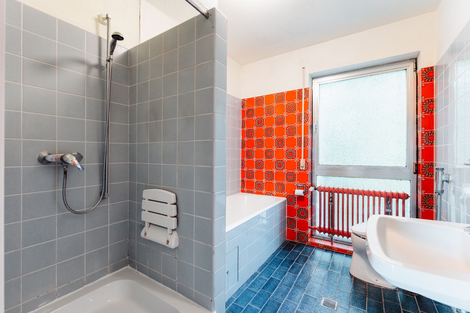 Badezimmer mit Dusche, Badewanne und auffälligen roten Fliesen an der Wand.