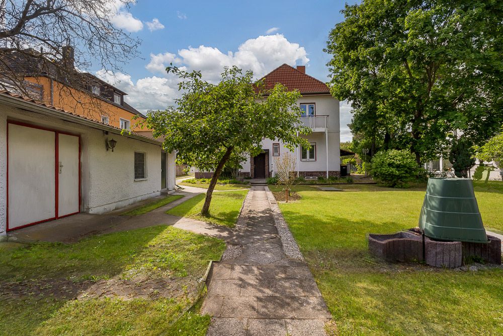 Garten mit Rasen, Baum, Weg, Haus im Hintergrund und Nebenbau links.