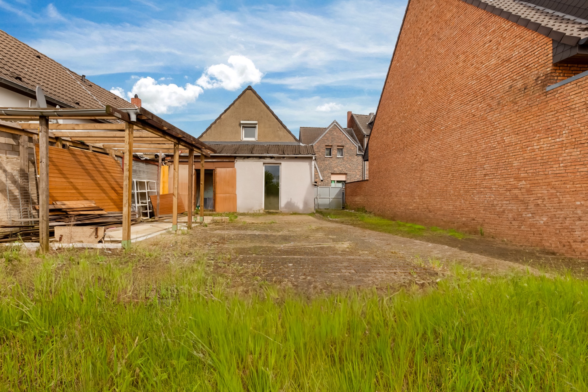 Hinterhof eines Wohnhauses mit Rasen, Holzüberdachung und gemauerter Wand.