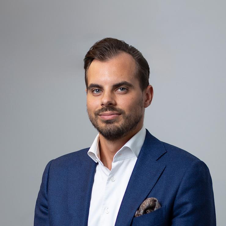 Ein Mann im blauen Anzug sitzt vor einem grauen Hintergrund.