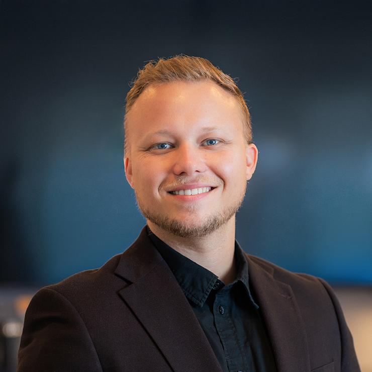 Ein junger Mann in einem blauen Anzug steht draußen und lächelt in die Kamera.