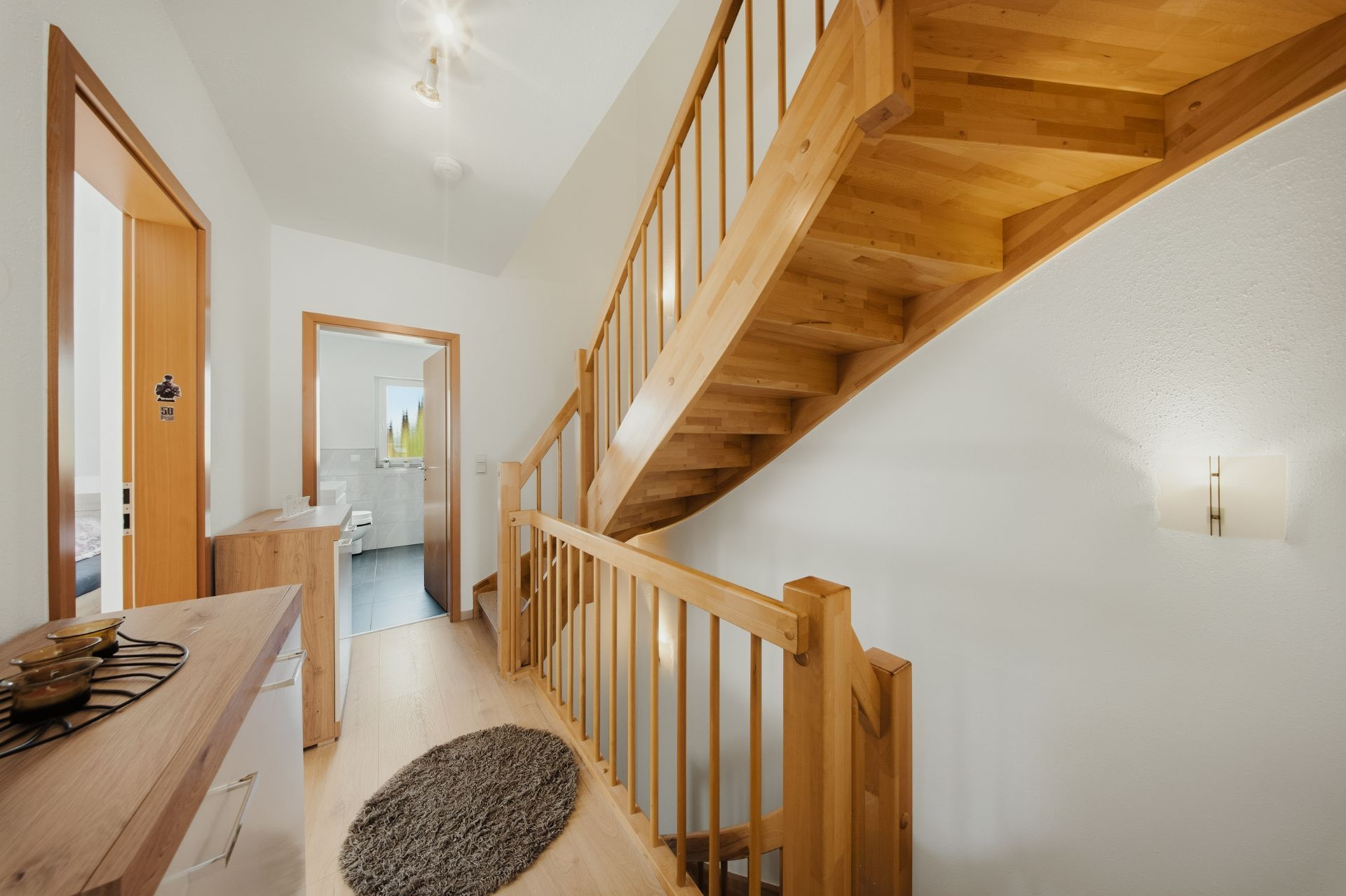 Heller Flur mit Holztreppe, Teppich und Zugang zu mehreren Räumen.