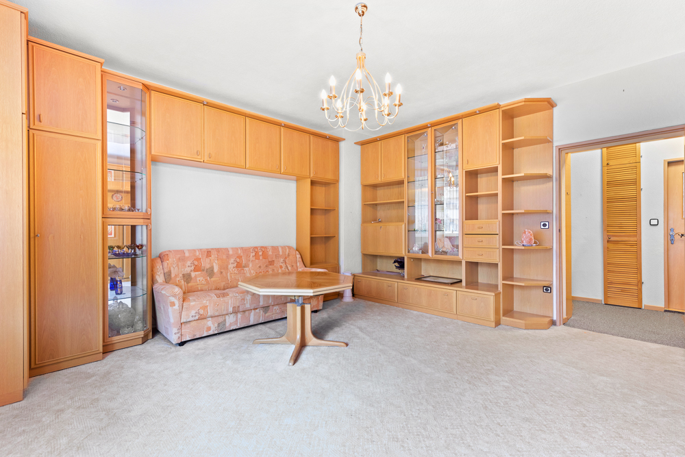 Wohnzimmer mit heller Schrankwand, Sofa, Couchtisch und Kronleuchter.