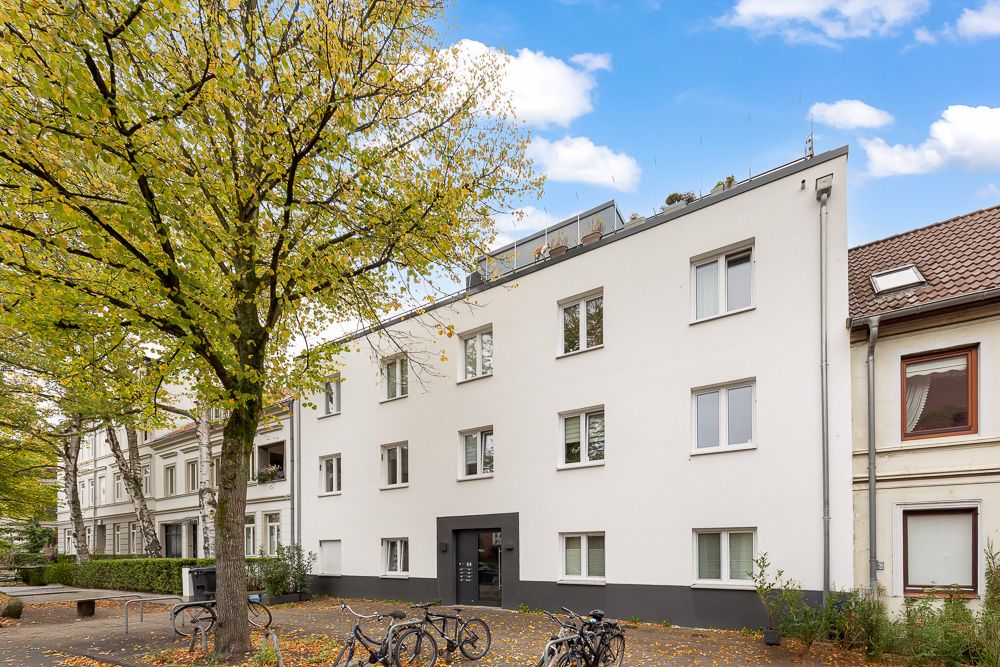 Modernes, weißes Wohnhaus mit mehreren Fenstern und Fahrrädern vor dem Eingang.