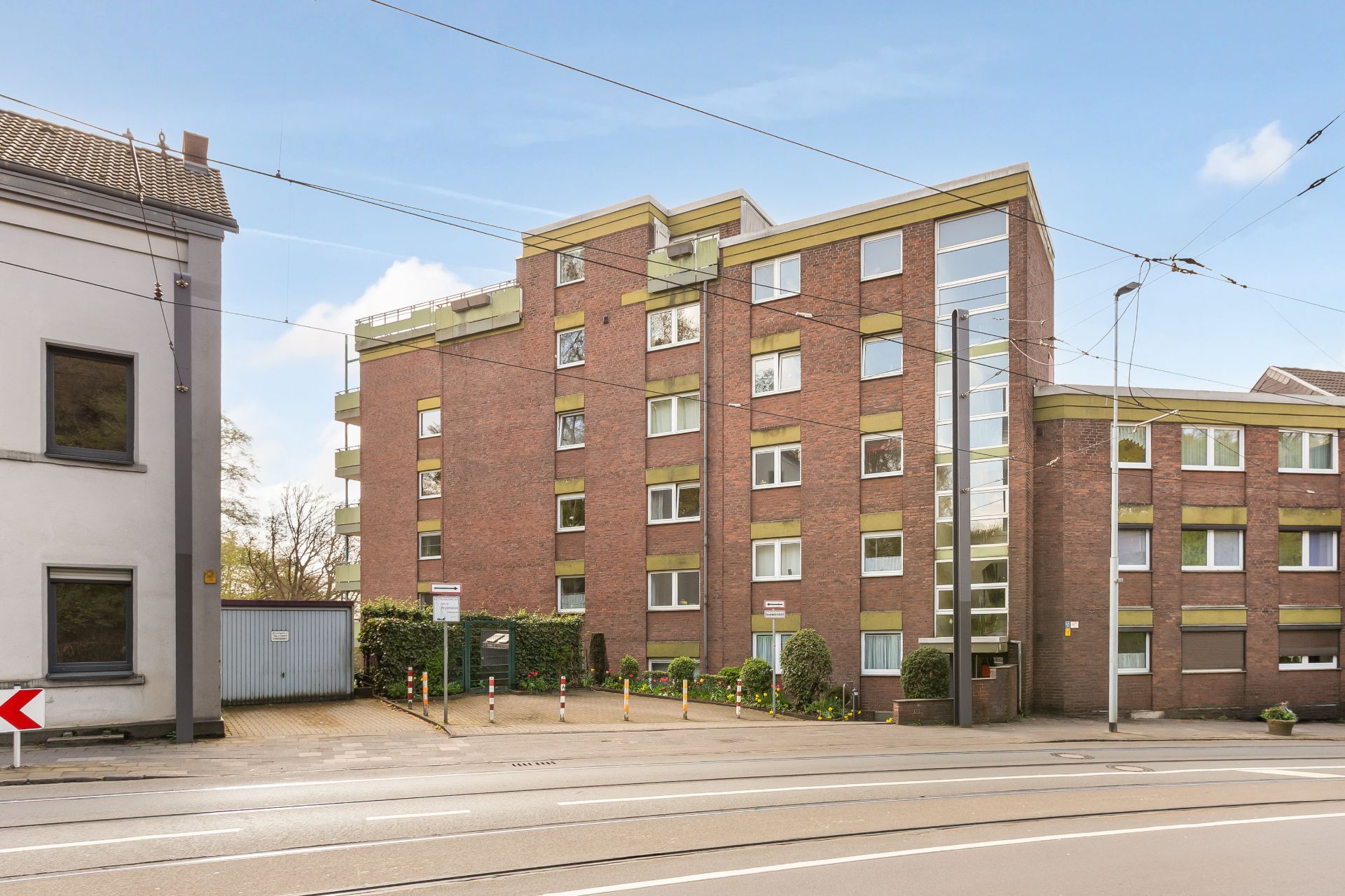 Mehrstöckiges Wohnhaus aus rotem Backstein mit vielen Fenstern und kleinem Parkplatz davor.