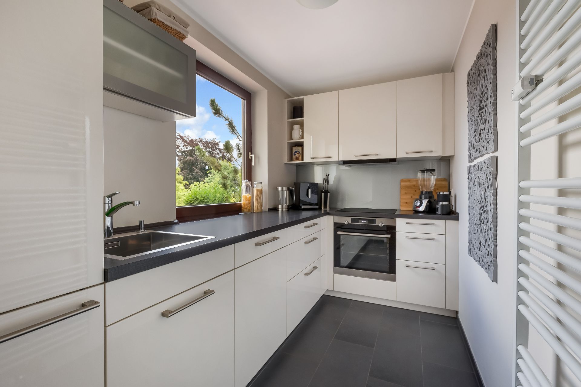 Moderne Küche mit weißen Schränken, großem Fenster und verschiedenen Küchengeräten.