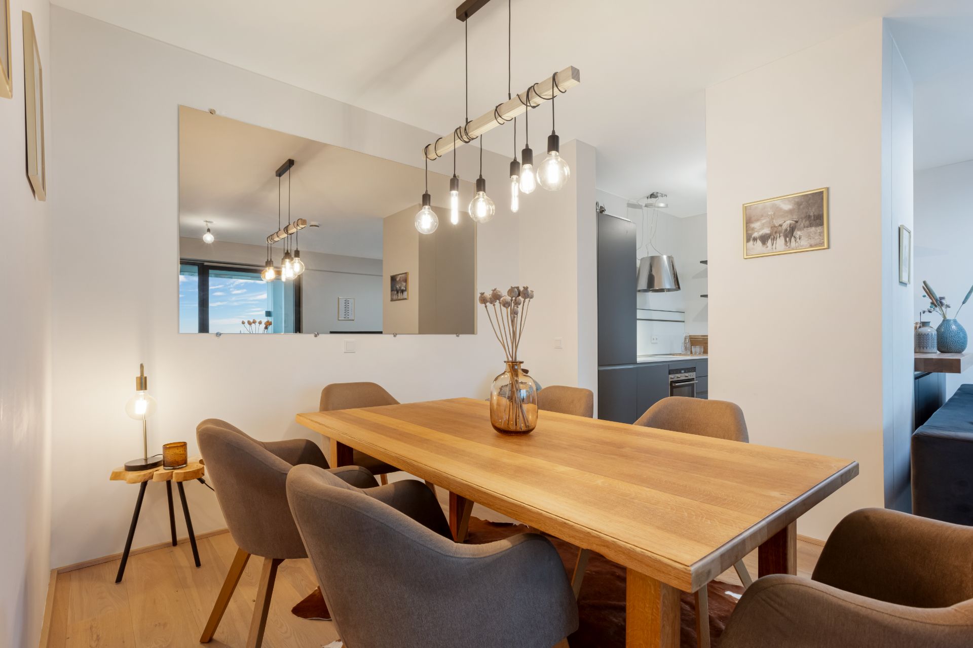 Essbereich mit Holztisch, sechs Stühlen und moderner Hängelampe, Küche im Hintergrund.