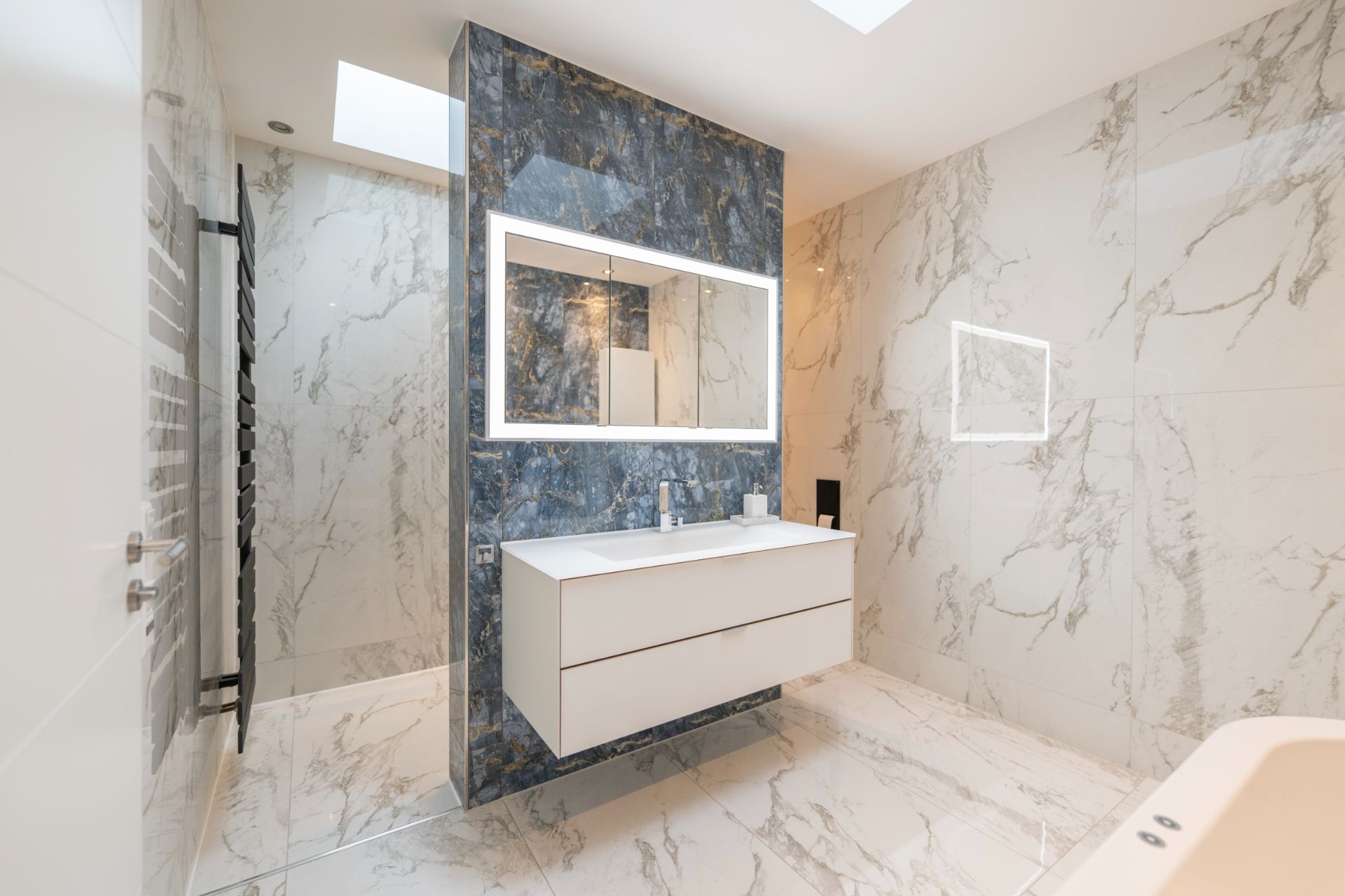 Modernes Badezimmer mit Marmorfliesen, großem Spiegel und Waschbecken mit weißem Unterschrank.