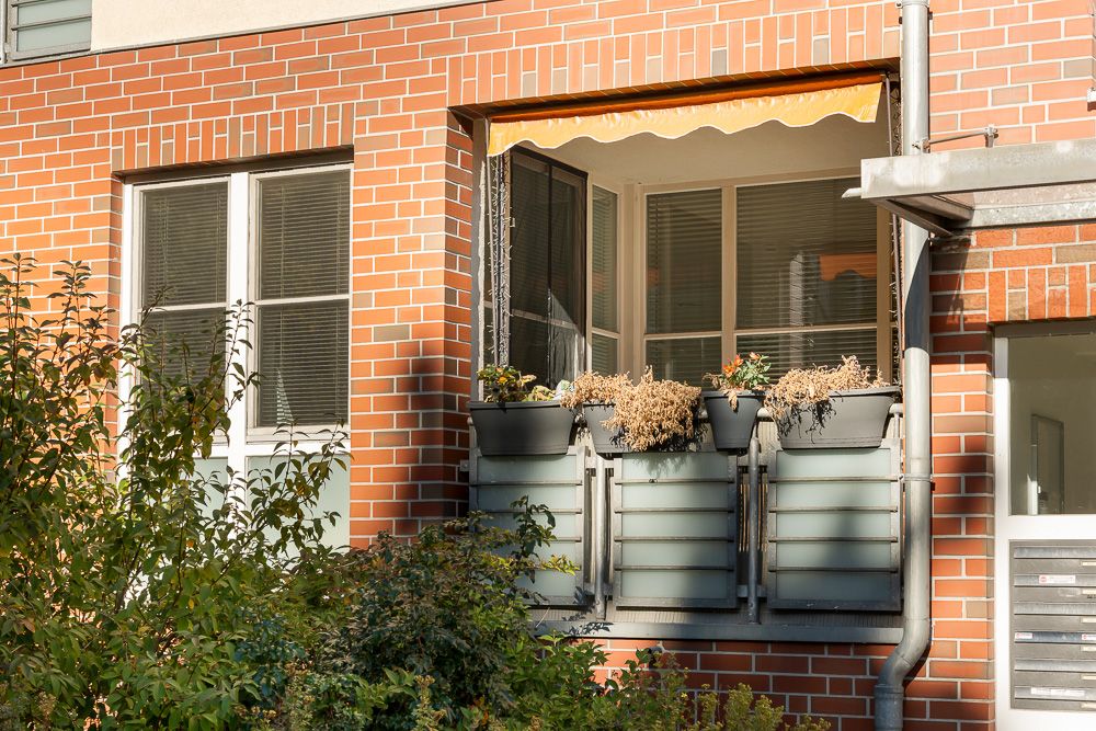 Kleiner Balkon mit Blumenkästen an einer rot verklinkerten Hauswand.