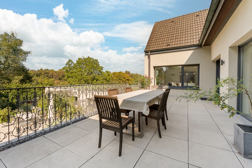 Große Terrasse mit Esstisch und Stühlen, Ausblick auf Bäume, angrenzend an ein Wohnhaus.