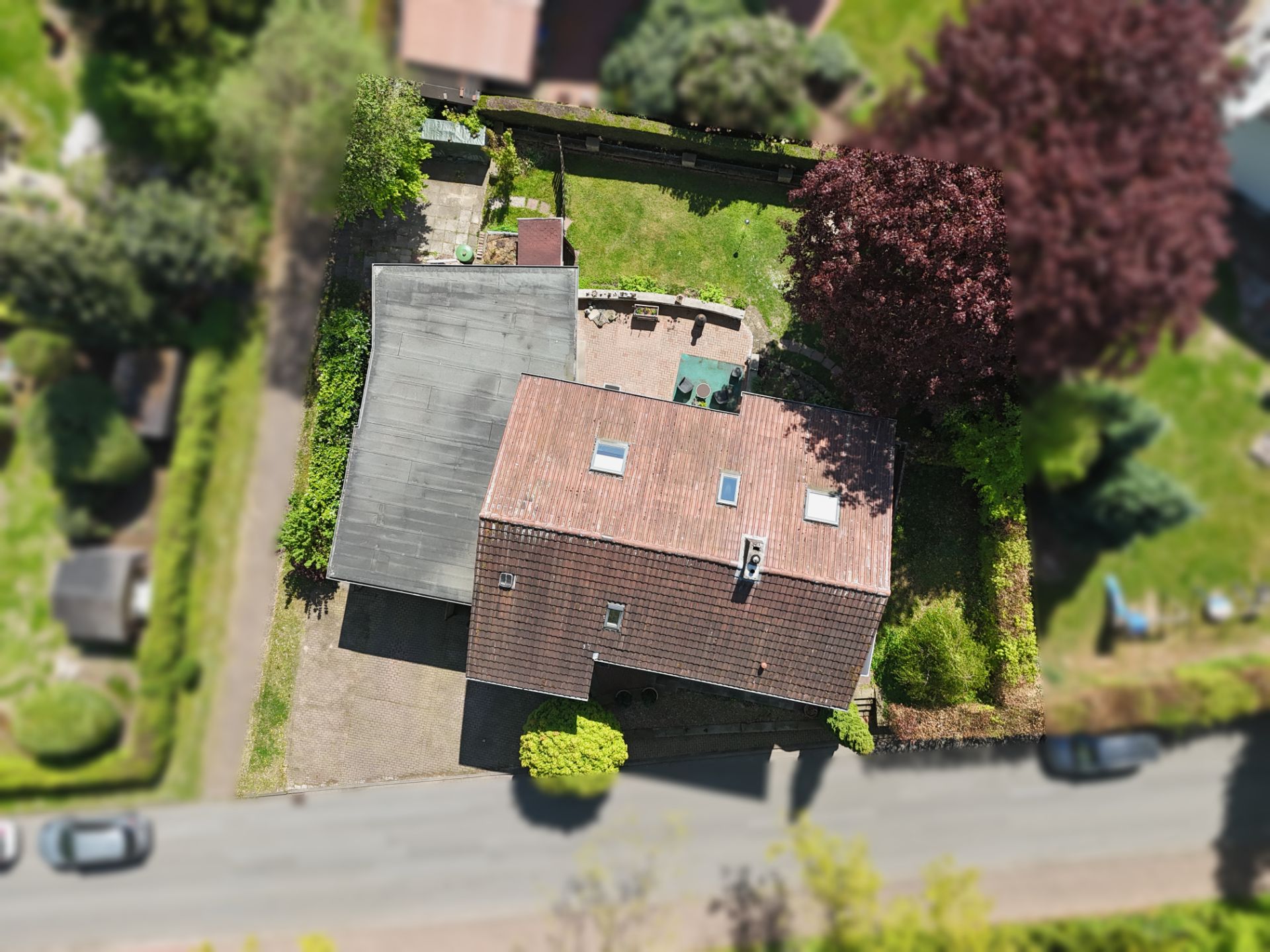 Luftaufnahme eines Wohnhauses mit Garten und Terrasse, umgeben von Bäumen und einer Straße.