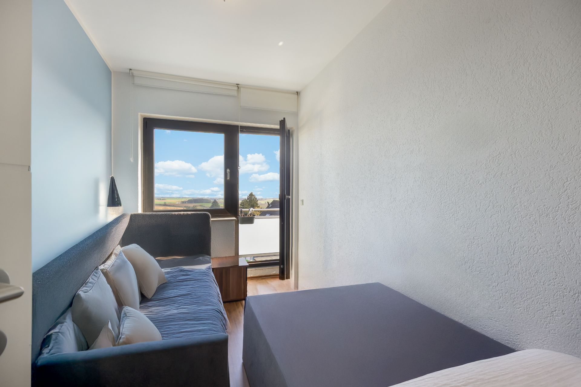 Kleines Zimmer mit Sofa, Bett und Glastür zu einem Balkon mit Ausblick auf Landschaft.