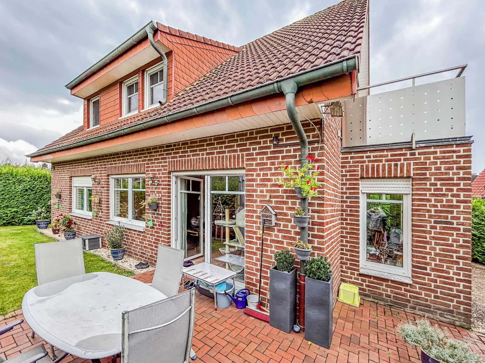 Backsteinwohnhaus mit Terrasse, Gartentisch und Stühlen im Gartenbereich.