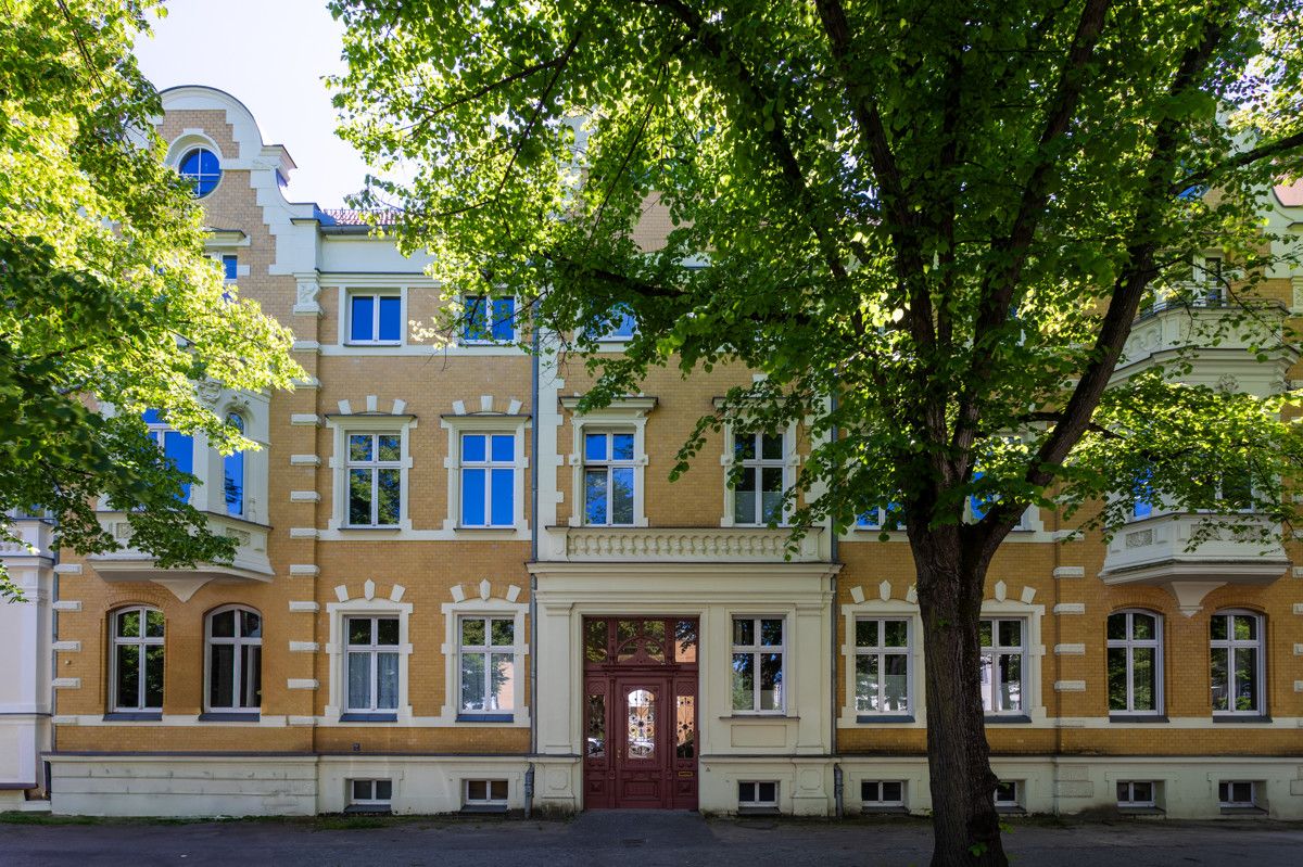 Fassadenansicht eines gelben Wohnhauses mit vielen Fenstern und Bäumen davor.
