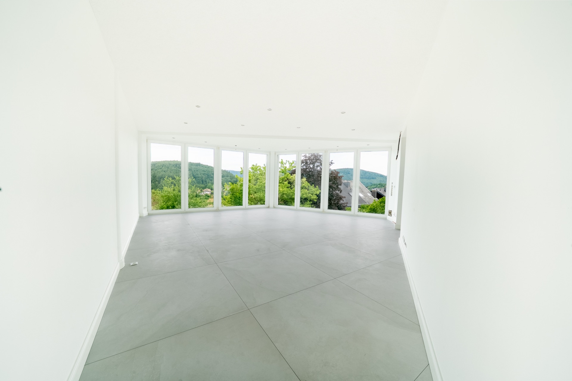 Leerer, heller Raum mit großen Fenstern und Blick ins Grüne.
