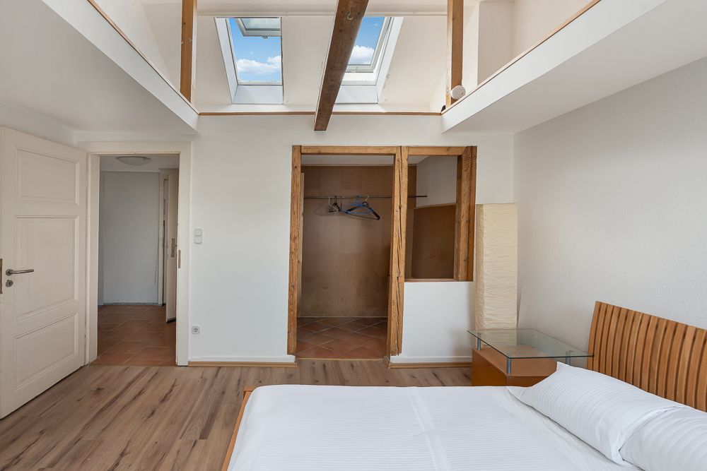 Helles Schlafzimmer mit Holzboden, Bett, offenem Kleiderschrank und Dachfenstern.