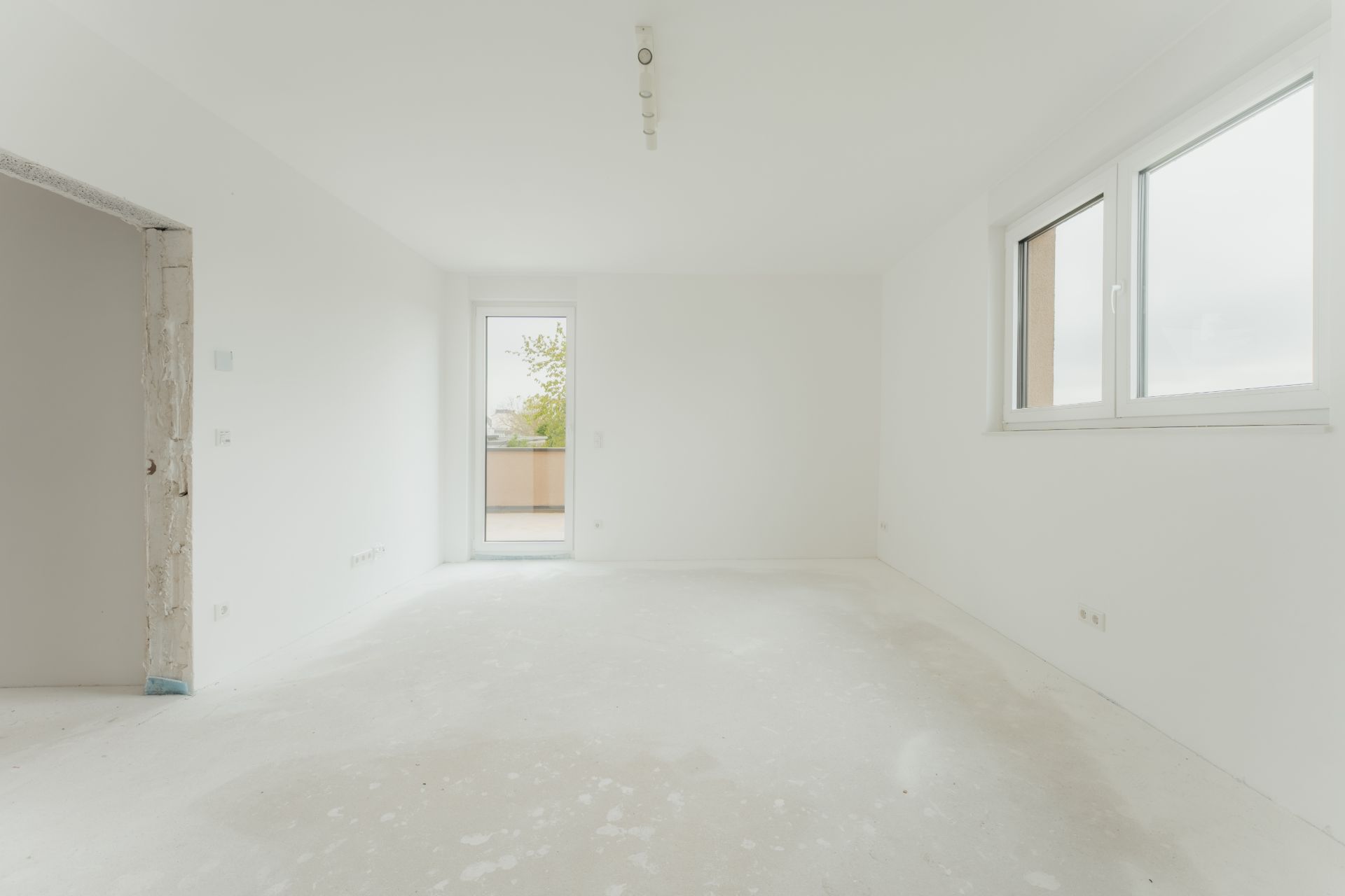 Leerer, weiß gestrichener Raum mit großen Fenstern und Tür zu einem Balkon.