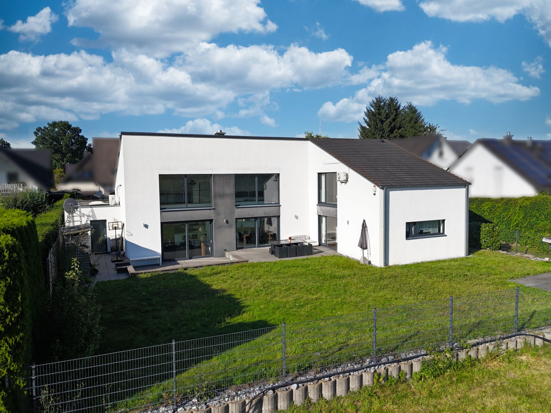 Modernes, weißes Wohnhaus mit großen Fenstern und Garten, aufgenommen bei Tageslicht.