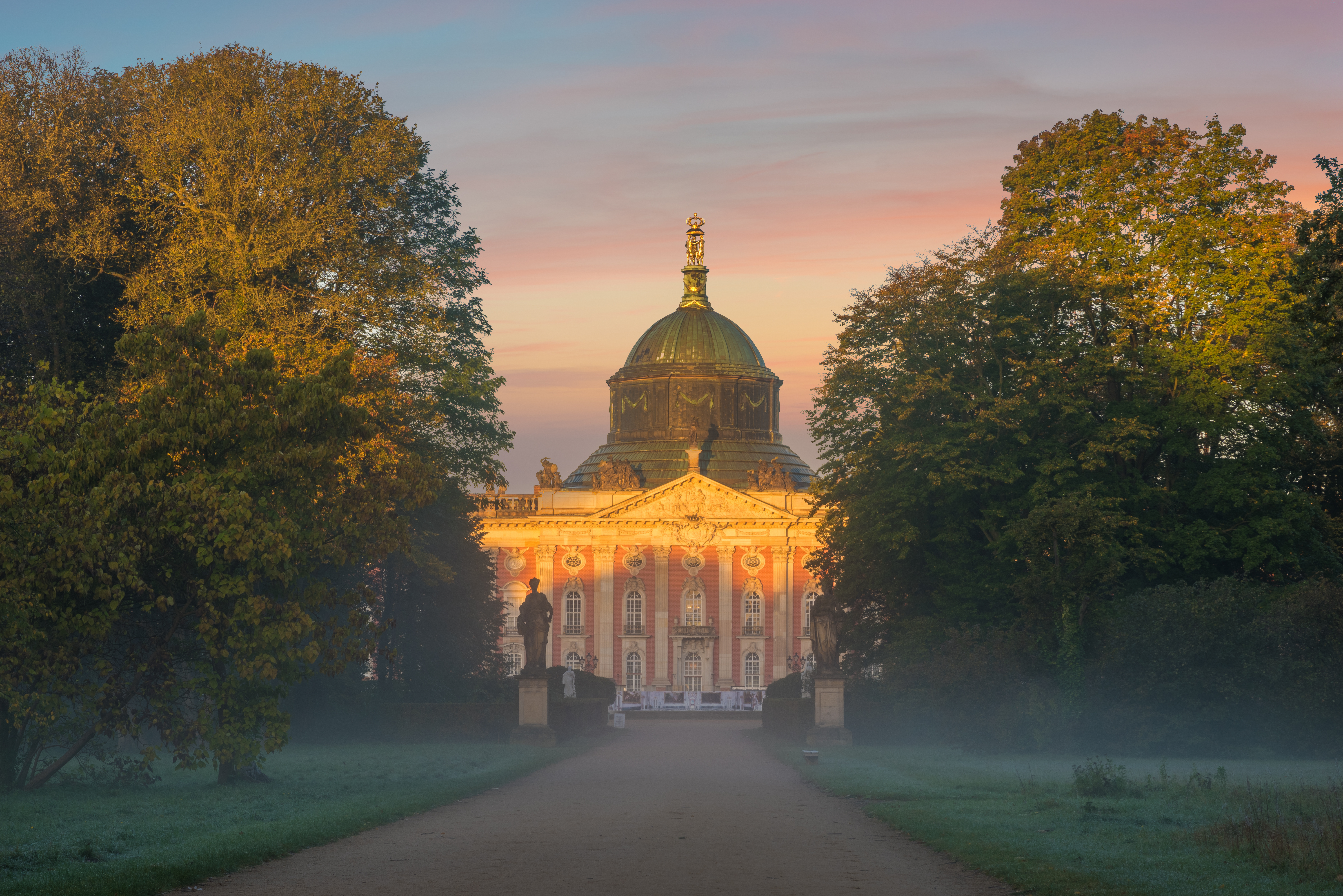 Großes historisches Gebäude mit Kuppel, flankiert von Bäumen bei Sonnenaufgang.