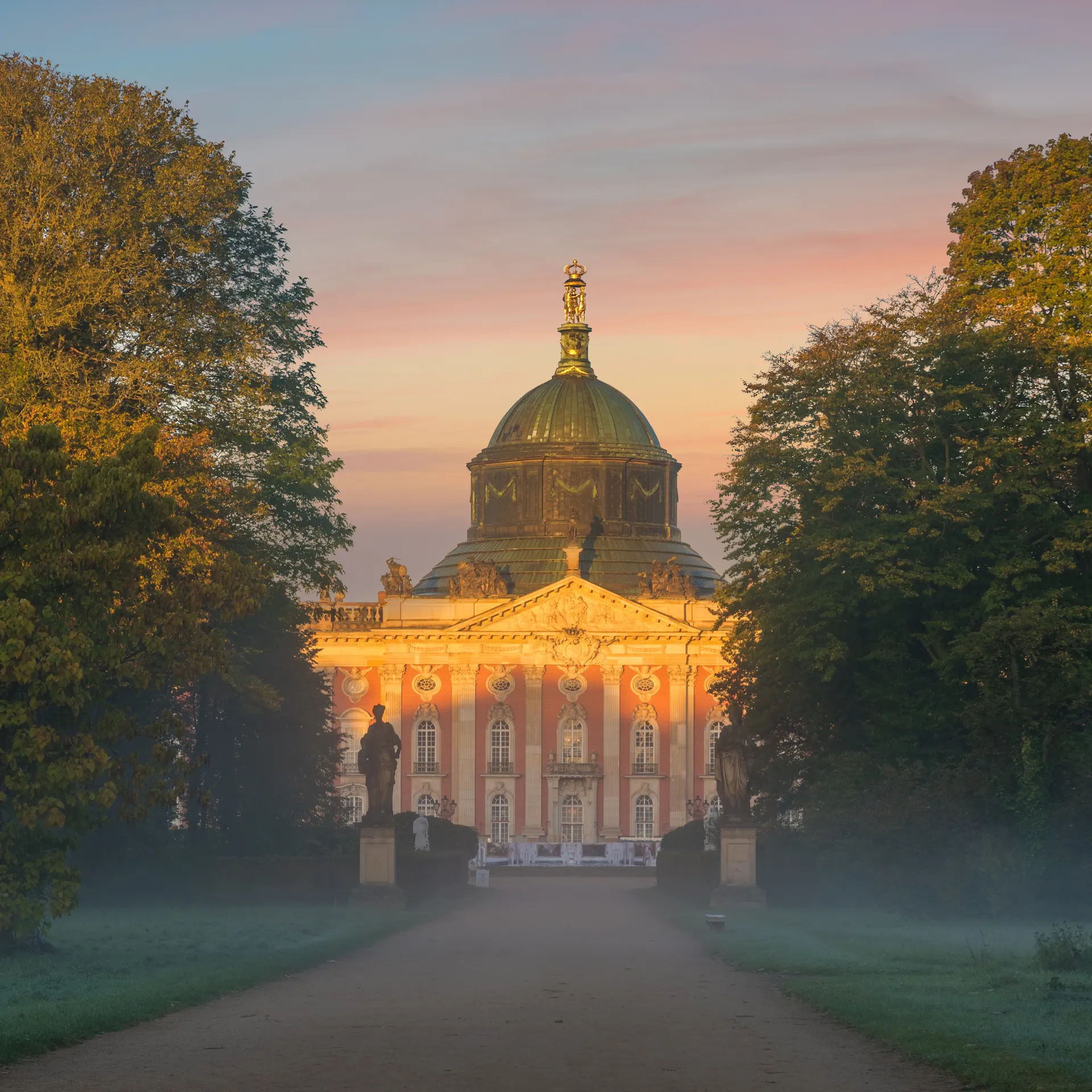 Großes historisches Gebäude mit Kuppel, flankiert von Bäumen bei Sonnenaufgang.