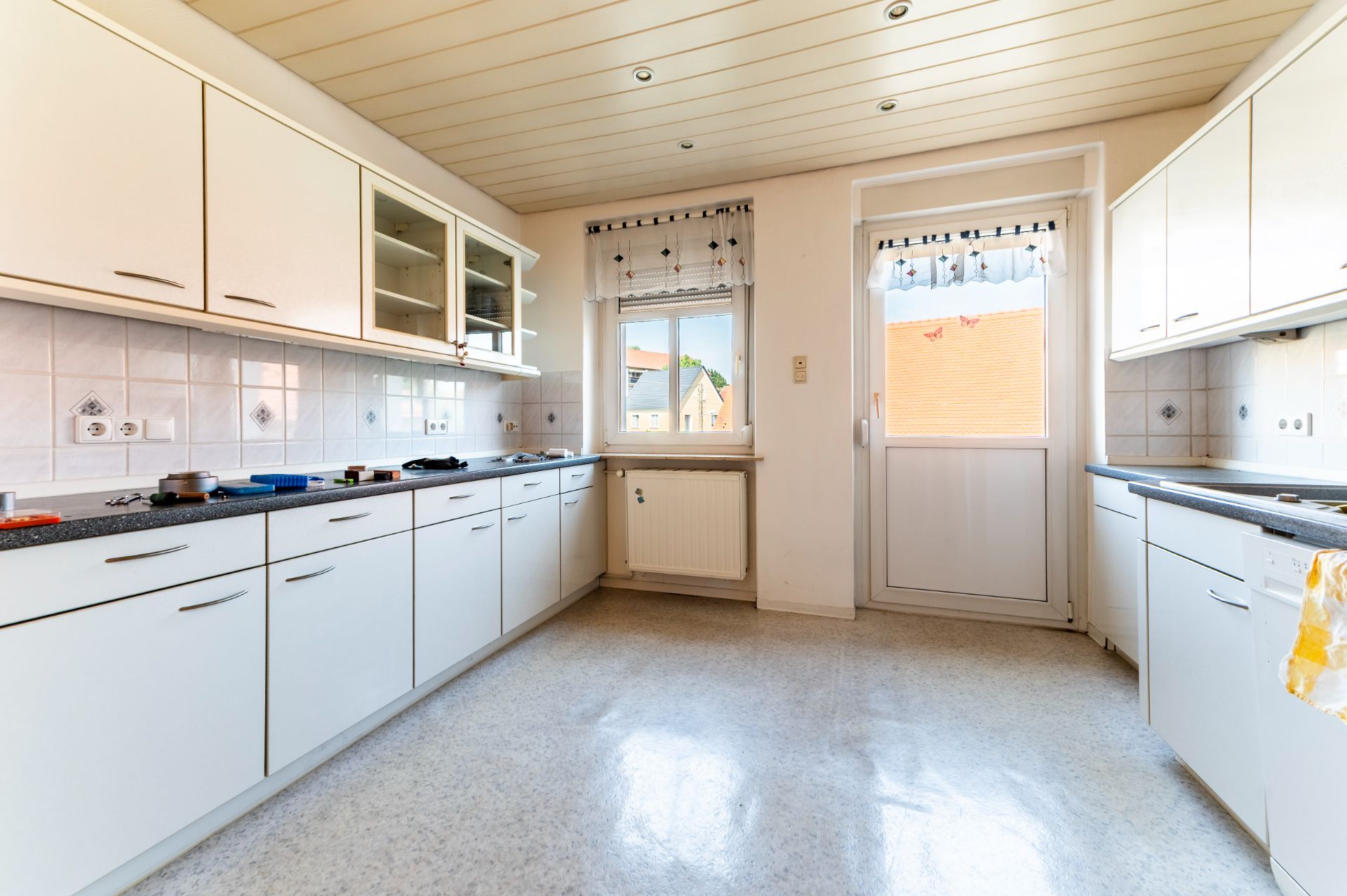 Helle Küche mit weißen Schränken, Fenster und Tür zum Außenbereich.
