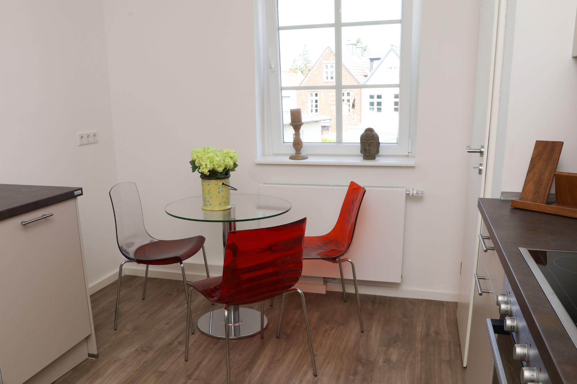 Kleine Küche mit rundem Glastisch, drei Stühlen und Fenster.