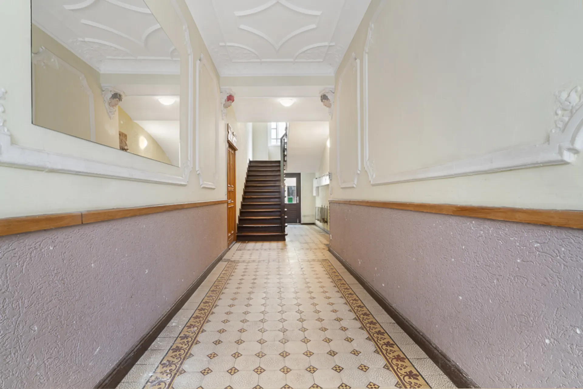 Heller Hausflur mit gemustertem Fliesenboden, Spiegel und Treppe am Ende.