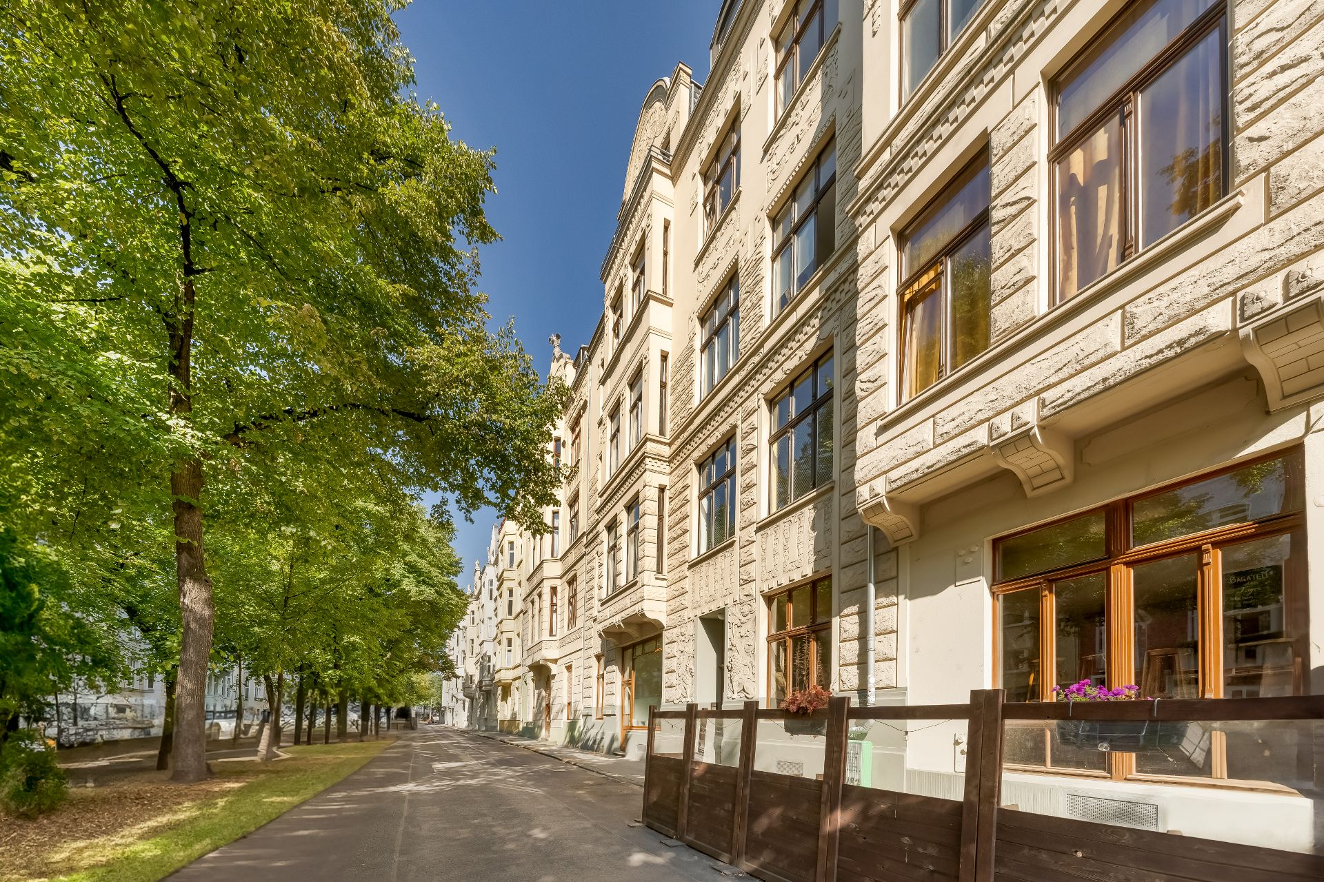 Wohnhaus mit hellen Fassaden an einer baumbestandenen Straße bei sonnigem Wetter.